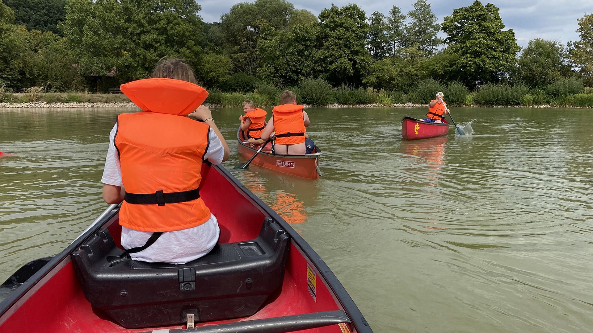 Fünf Pfadfinder in orangenen Schwimmwesten fahren auf dem See in Wörnitz in Kanadiern.